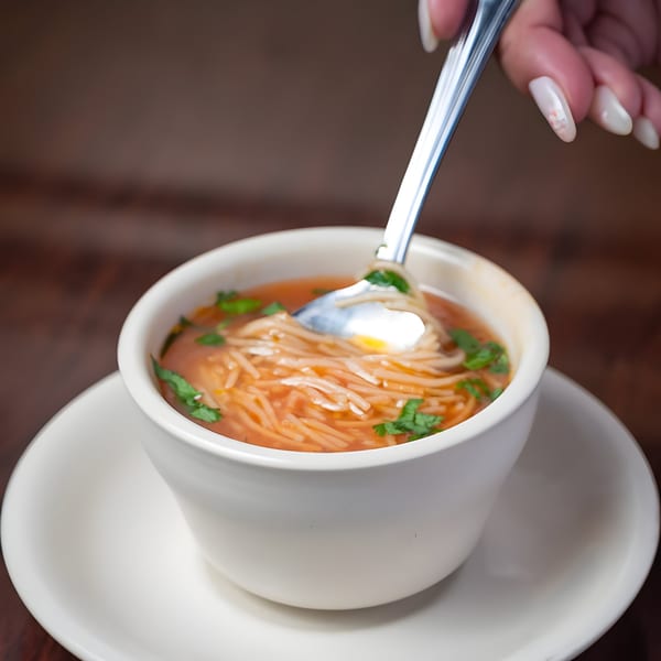 A hand stirs a bowl of Mexican noodle soup with cilantro and a dollop of sour cream.