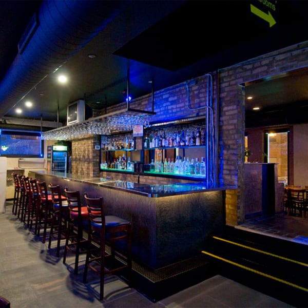 A long bar with stools, illuminated bottles, and blue lighting in Cesar's Killer Margaritas.