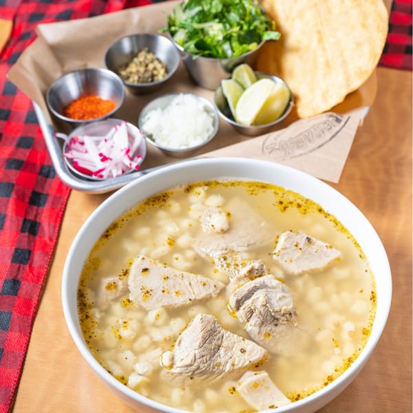 A bowl of Mexican pozole with pork and hominy, served with various toppings.