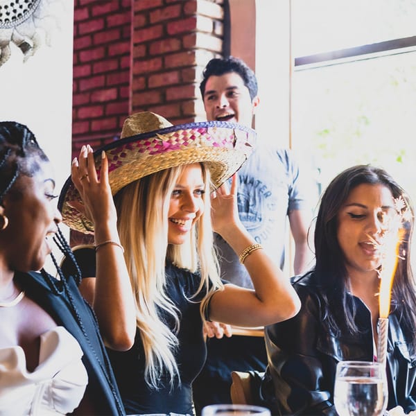 Three women and a man celebrating a birthday with a sombrero and sparkler at Cesar's.