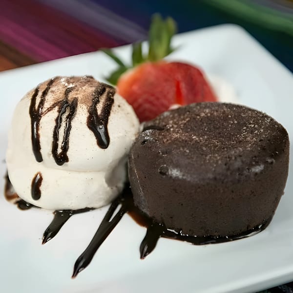 Chocolate lava cake with vanilla ice cream, chocolate drizzle, and a strawberry on a white plate.