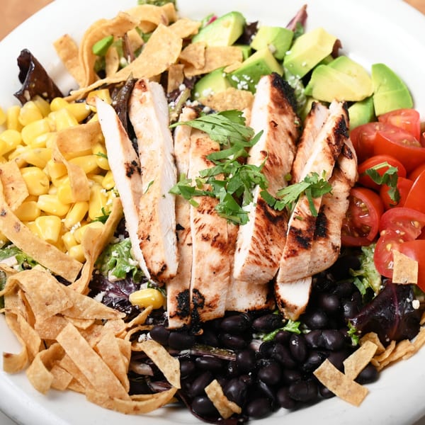 Grilled chicken salad with corn, black beans, avocado, tomatoes, and tortilla strips.