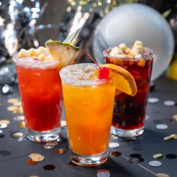 Three colorful margaritas, garnished with fruit and salt, on a confetti-strewn table.