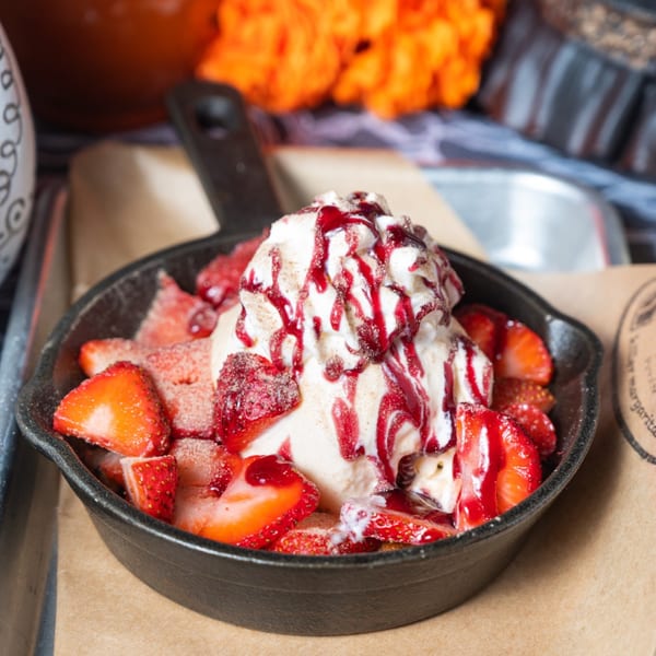 Skillet of strawberries, vanilla ice cream, whipped cream, and berry sauce, a Mexican dessert.