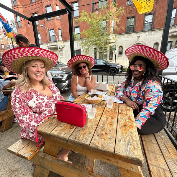 Three women wearing sombreros and smiling at a wooden picnic table on Cesar's Killer Margaritas patio.