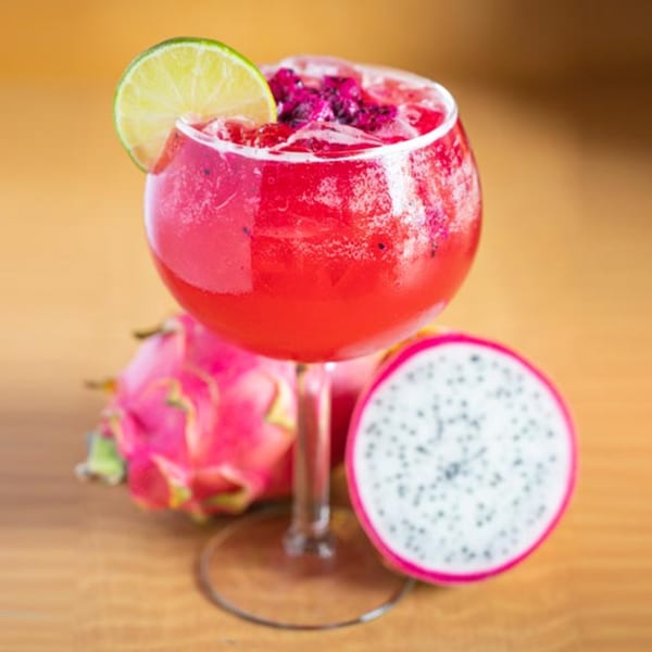 A vibrant red dragon fruit margarita with a lime wedge, surrounded by fresh dragon fruit.